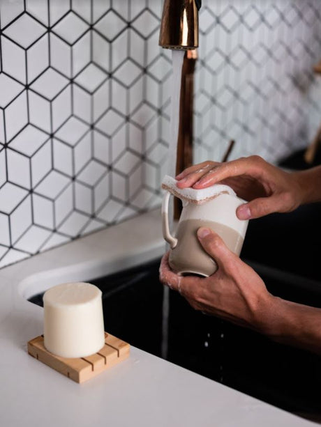A person's hands washing a mug with a bar of Meliora Dish Soap.