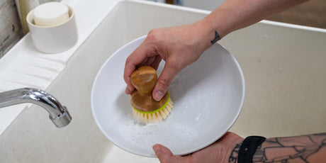 A photo of a person scrubbing a bowl with a soapy dish brush.