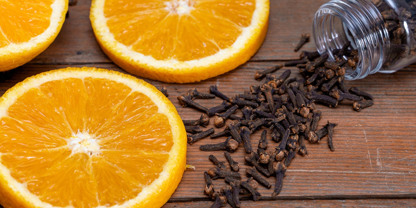 A photo of orange slices and whole cloves on a wooden table.