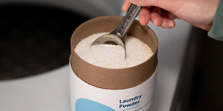 A person's hand scooping Meliora Laundry Powder from a canister.
