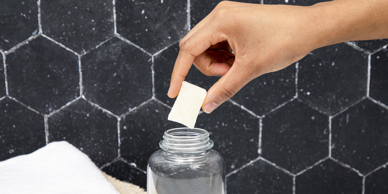 A hand placing a solid soap tablet in an open container.