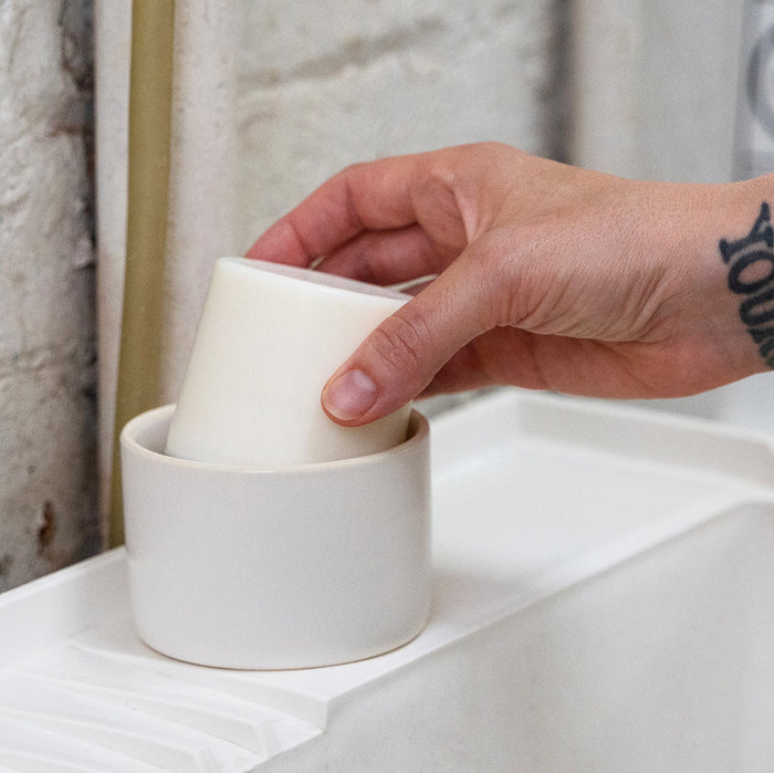 A photo of a person placing a dish soap bar in a ceramic soap dish.