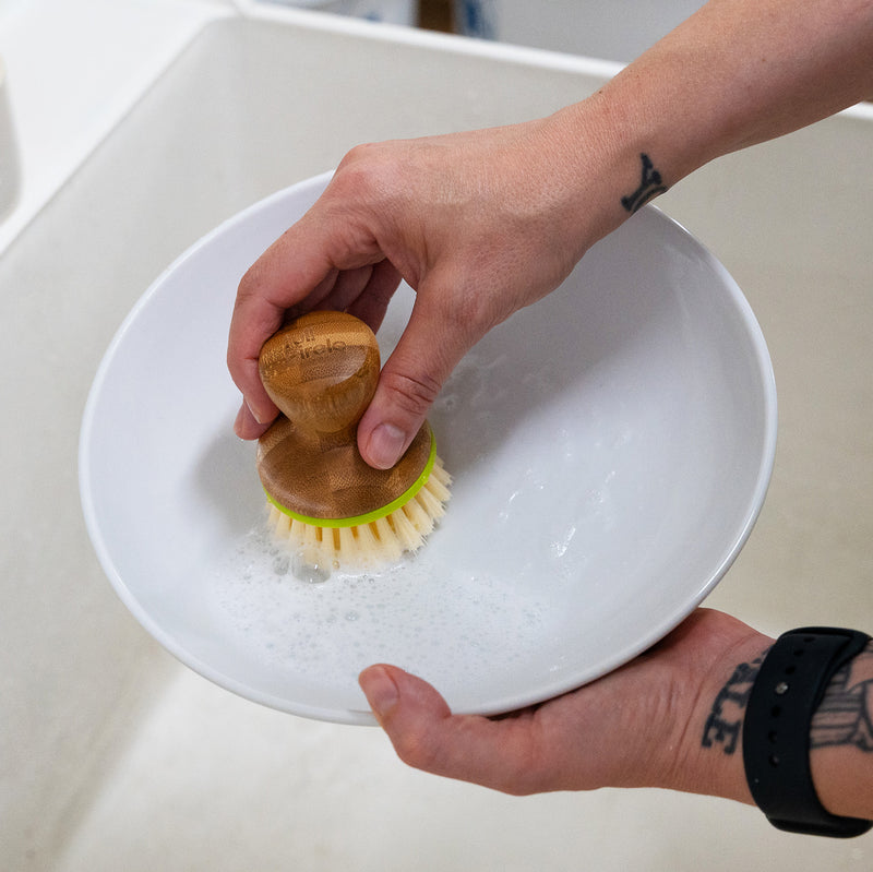 A photo of a person scrubbing a bowl with a soapy dish brush.