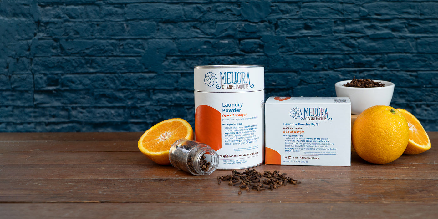 Spiced Orange Laundry Powder with sliced oranges and whole cloves on a wooden table with a blue brick backdrop.