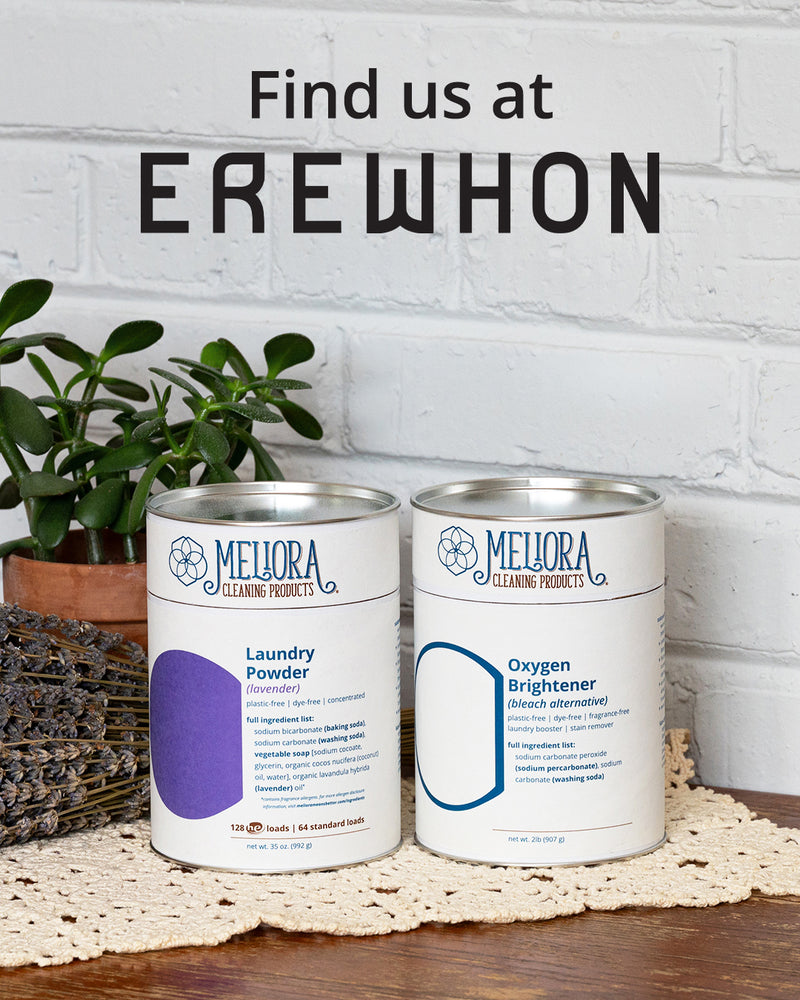 A photo of Meliora Laundry Powder and Oxygen Brightener canisters on a wooden surface with a plant and white brick wall in the background, featuring the text 'Find us at Erewhon'.