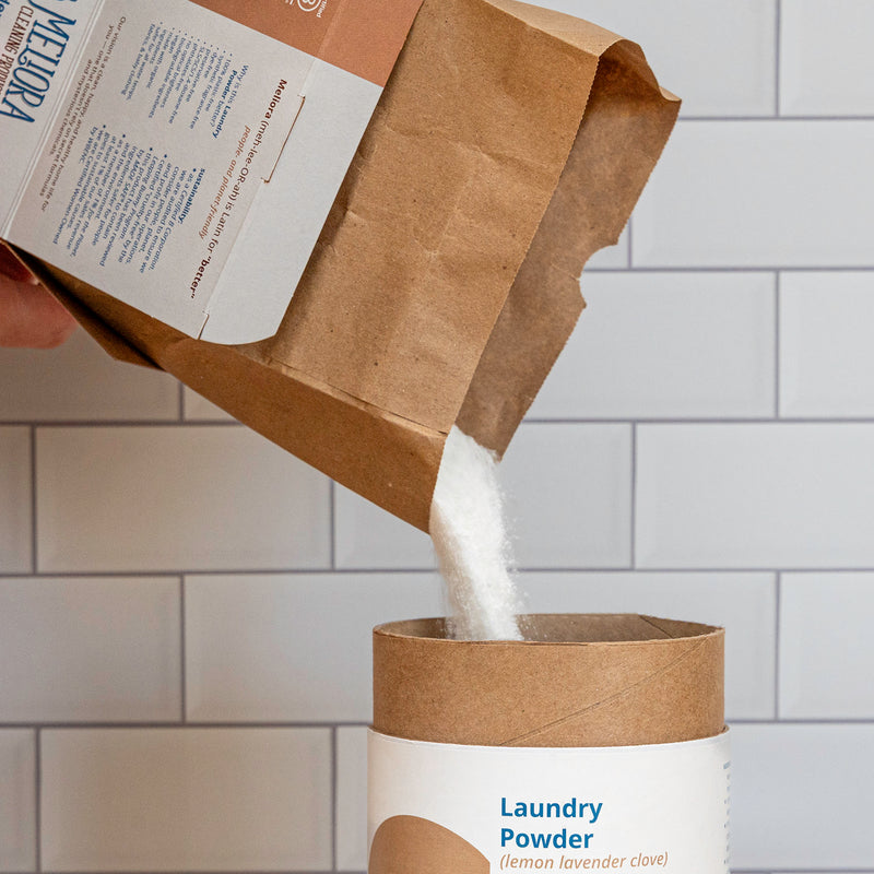 A photo of Meliora all-paper Laundry Powder Refill boxes pouring powder into a Laundry Powder canister.