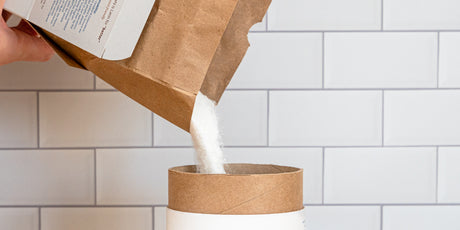 A photo of a person pouring Meliora Laundry Powder from a refill box into a canister.
